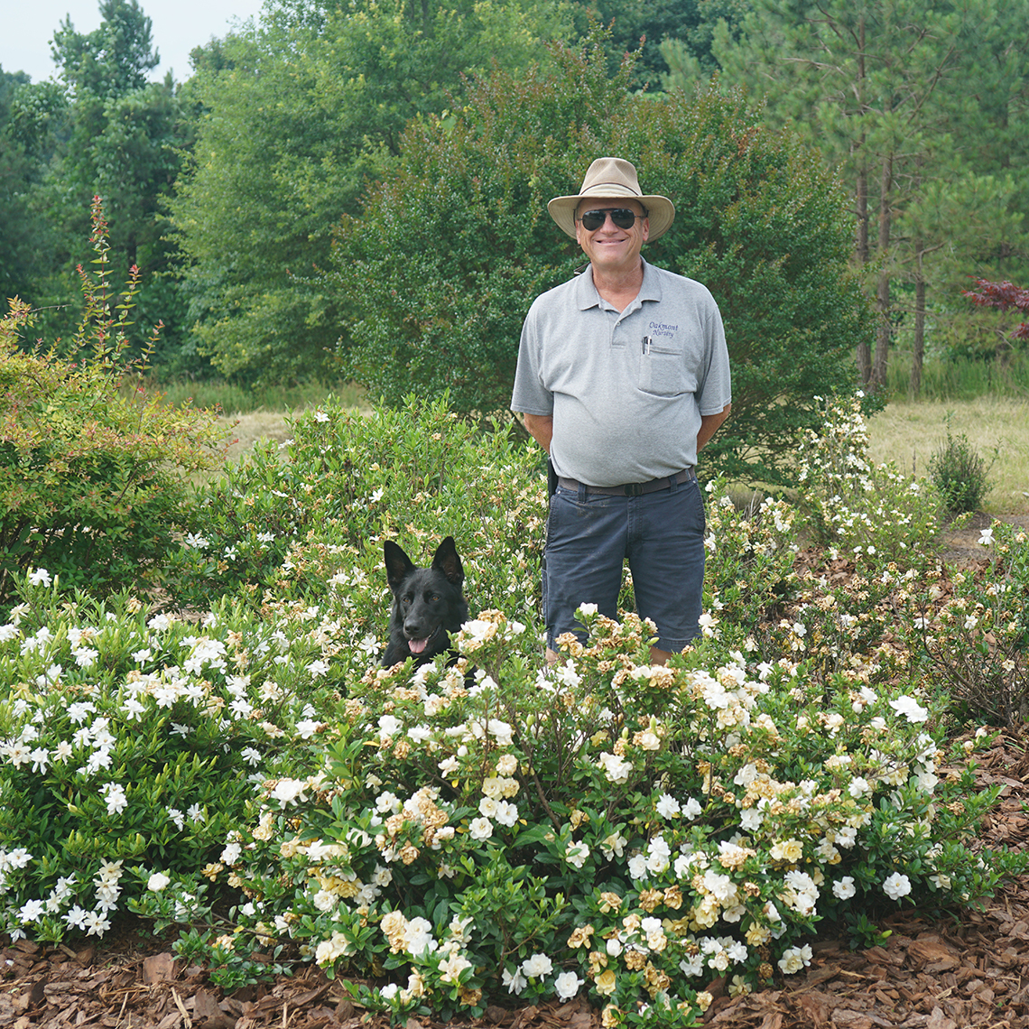 the breeder and a german shepherd dog standing behind a Steady As She Goes gardenia 