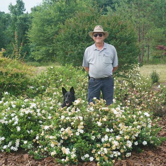 the breeder and a german shepherd dog standing behind a Steady As She Goes gardenia 